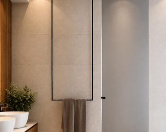 May include: A tall, rectangular black metal towel rack mounted on a beige tiled wall, featuring a single horizontal bar at the bottom holding two folded brown towels, positioned next to a tall gray door and a wooden vanity with white sinks.