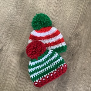 May include: Two crocheted hats with pom-poms in red, white, and green. The hats have a striped pattern.