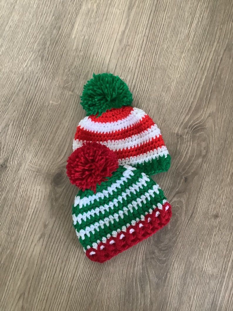 May include: Two crocheted hats with pom-poms in red, white, and green. The hats have a striped pattern.