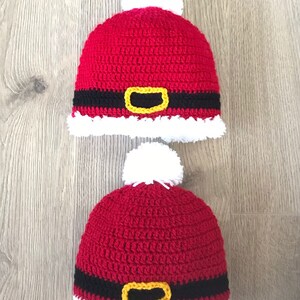 May include: Two red crocheted Santa hats with white pom-poms and black and yellow belts.