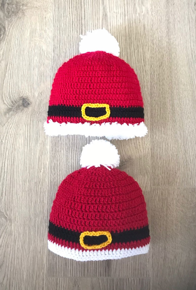 May include: Two red crocheted Santa hats with white pom-poms and black and yellow belts.