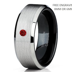 Könnte beinhalten: Ein silberner und schwarzer Ring aus Wolframcarbid mit einem roten Edelstein. Der Ring ist mit "TUNGSTEN CARBIDE" graviert.