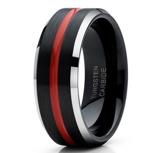 May include: A black tungsten carbide ring with a red stripe and a silver band. The ring is engraved with the words "TUNGSTEN CARBIDE".