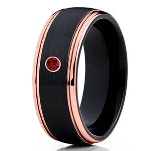 Puede incluir: Un anillo de carburo de tungsteno negro con una banda de oro rosa y una sola piedra roja.