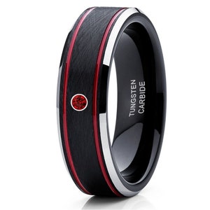 May include: Black tungsten carbide ring with a red inlay and a single red gemstone. The ring has a beveled edge and is engraved with "TUNGSTEN CARBIDE".