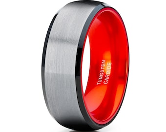 May include: A silver tungsten carbide ring with a black outer edge and a red inner edge. The words "TUNGSTEN CARBIDE" are engraved on the red inner edge.