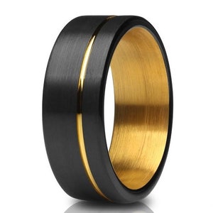 May include: A black tungsten carbide ring with a gold inlay. The ring has a brushed finish and a bevelled edge.
