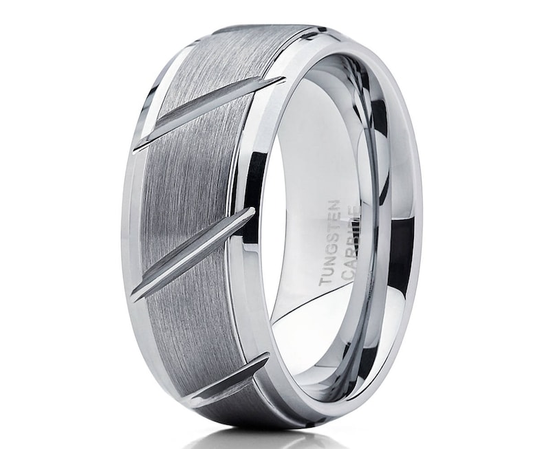 May include: A silver tungsten carbide ring with a brushed finish and a beveled edge. The ring has a grooved design on the top and the words "TUNGSTEN CARBIDE" engraved on the side.