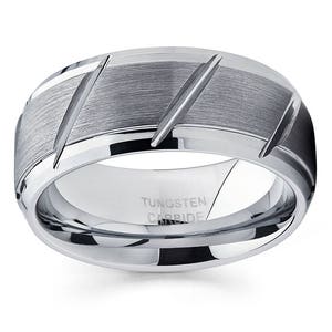 May include: A silver tungsten carbide ring with a brushed finish and diagonal grooves. The ring is engraved with "TUNGSTEN CARBIDE".