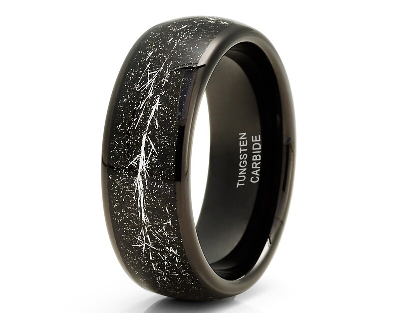 May include: A black tungsten carbide ring with a white speckled finish and a white lightning bolt design. The inside of the band is engraved with "TUNGSTEN CARBIDE".
