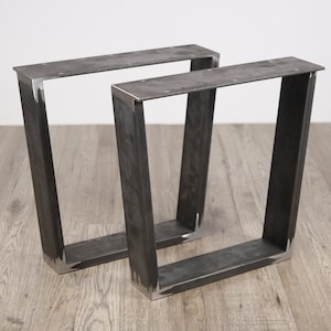 Peut inclure: Deux pieds de table en métal noir avec un design légèrement incliné. Les pieds sont en métal épais et ont un aspect brut et industriel.