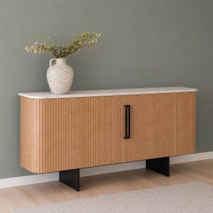 Könnte beinhalten: Ein hellbraunes Sideboard aus Holz mit weißer Oberseite und abgerundeten Kanten, ausgestattet mit vertikalen Lamellen, zwei schwarzen vertikalen Griffen und schwarzen Standfüßen. Darauf steht eine strukturierte, cremeweiße Keramikvase mit Eukalyptuszweigen.