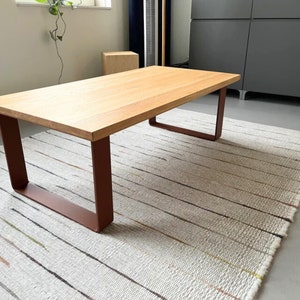 Puede incluir: Una mesa de centro de madera clara con una tapa rectangular y un marco de metal oxidado. La mesa está sobre una alfombra rayada blanca y crema.