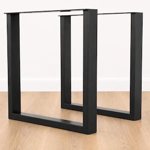 Pode incluir: Um par de pernas de mesa de metal preto fosco com um design retangular em forma de U. Cada perna é construída a partir de barras de aço planas e grossas com um acabamento liso e orifícios de montagem pré-perfurados na barra superior.