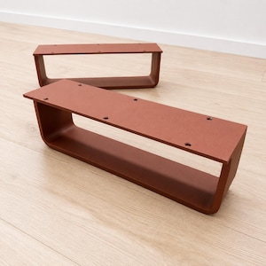 Op de afbeelding: Twee rechthoekige, terracotta-kleurige metalen meubelpoten met een U-vormig profiel. Elke poot heeft een plat bovenoppervlak met vier voorgeboorde ronde gaten voor montage en afgeronde hoeken aan de onderkant van de frameconstructie.