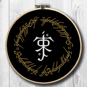 May include: Cross-stitch embroidery in a wooden hoop featuring a black background with gold lettering and a white central symbol. The design is a circular pattern with text around the edge.