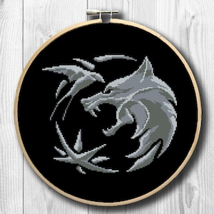 May include: A black and white embroidered design of a wolf's head in a circle, on a black fabric background. The wolf's head is facing left and has a sharp, pointed snout. The design is surrounded by a circle of stylized leaves.