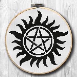 May include: A black and white cross-stitch design featuring a pentagram within a circle, surrounded by stylized sun rays. The design is set in a wooden embroidery hoop, perfect for wall decor or crafting projects.