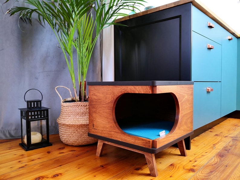 May include: A wooden pet bed with a blue cushion inside. The bed is shaped like a heart and has a dark brown finish. The bed is sitting on a wooden floor in front of a blue and black cabinet.