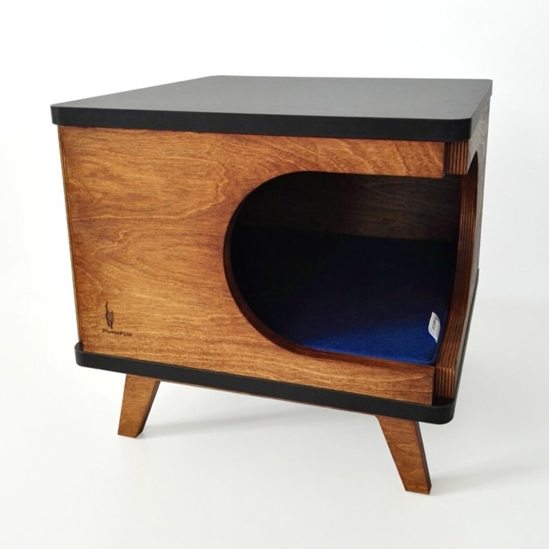 May include: A wooden cat bed with a black top and a blue cushion inside. The bed has a rounded opening and sits on four legs. The bed is labeled "Furever Fun".