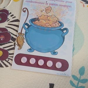 May include: A card with a cartoon illustration of a blue cauldron with bubbling orange potion, a broom, and the text "Reproduis la bonne recette pour confectionner la potion magique." Below the cauldron is a maroon rectangle with five white circles.