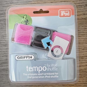 May include: A pink and black Griffin Tempo armband for the iPod shuffle, packaged in a clear plastic case. The packaging includes the text "Works with iPod" and "tempo shuffle".