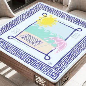Puede incluir: Mesa cuadrada de madera con un dise&ntilde;o de escena de playa en la parte superior. El dise&ntilde;o incluye un sol amarillo, un paraguas rosa y olas azules. La mesa tiene un borde de clave griega azul y blanco.