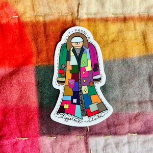 May include: A colorful sticker of a person wearing a patchwork coat with the text "CUT FROM A DIFFERENT CLOTH" around the edges.