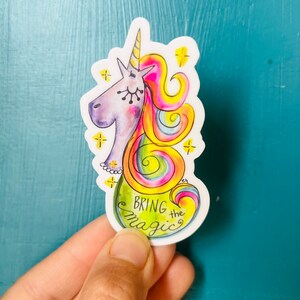 May include: A colorful sticker featuring a cartoon unicorn with a rainbow mane and tail. The unicorn is wearing a pearl necklace and the text "Bring the Magic" is written in a whimsical font.