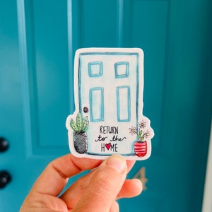 May include: A sticker featuring a watercolor illustration of a light blue door with the text "Return to the Home" and a red heart. The sticker also includes potted plants on either side of the door.