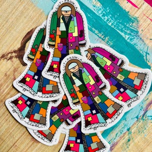 Pu&ograve; includere: Cinque adesivi colorati con un personaggio dei cartoni animati che indossa un cappotto di patchwork. Il testo sugli adesivi dice "Cut from a different cloth".
