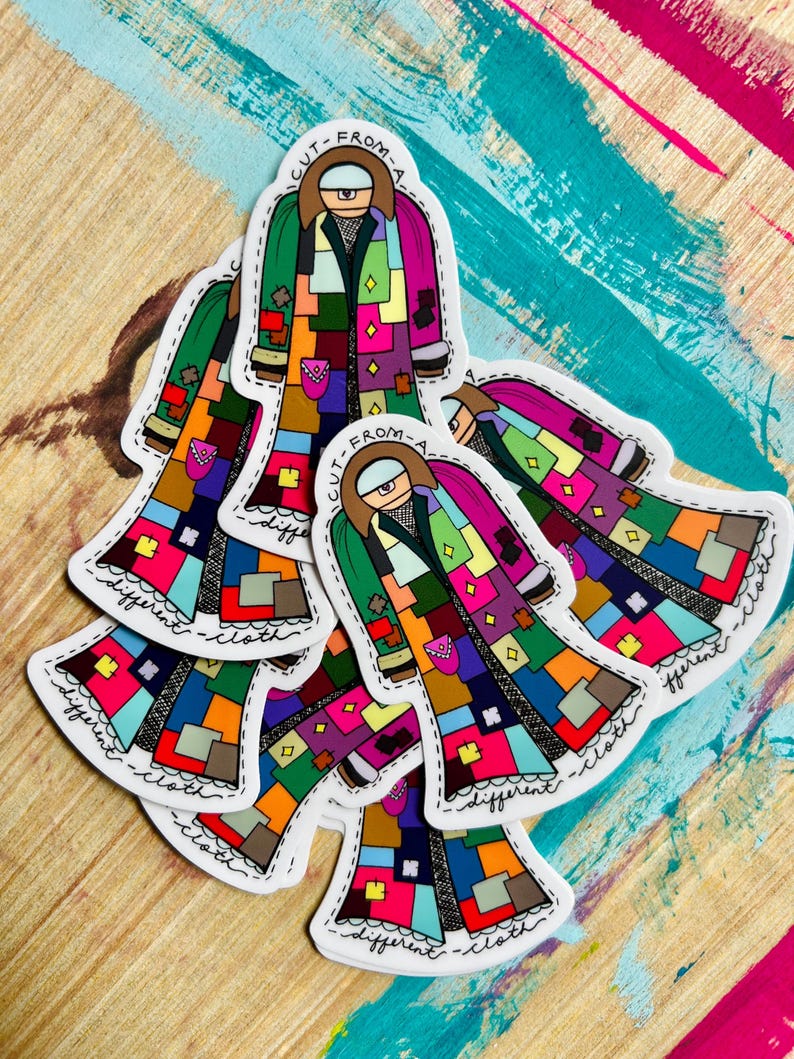 Pu&ograve; includere: Cinque adesivi colorati con un personaggio dei cartoni animati che indossa un cappotto di patchwork. Il testo sugli adesivi dice "Cut from a different cloth".
