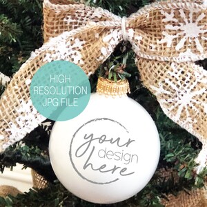 Könnte beinhalten: Weißer Weihnachtsbaumschmuck mit dem Text "your design here" in grauer Schrift. Der Schmuck hängt an einem grünen künstlichen Weihnachtsbaum mit einer Schleife aus Sackleinen mit weißen Schneeflocken.