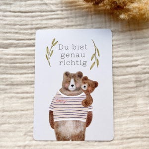 May include: A rectangular card with a watercolor illustration of two bears. The larger bear wears a striped shirt with the word "honey" on it. The smaller bear is hugging the larger bear. The text "Du bist genau richtig" is at the top.