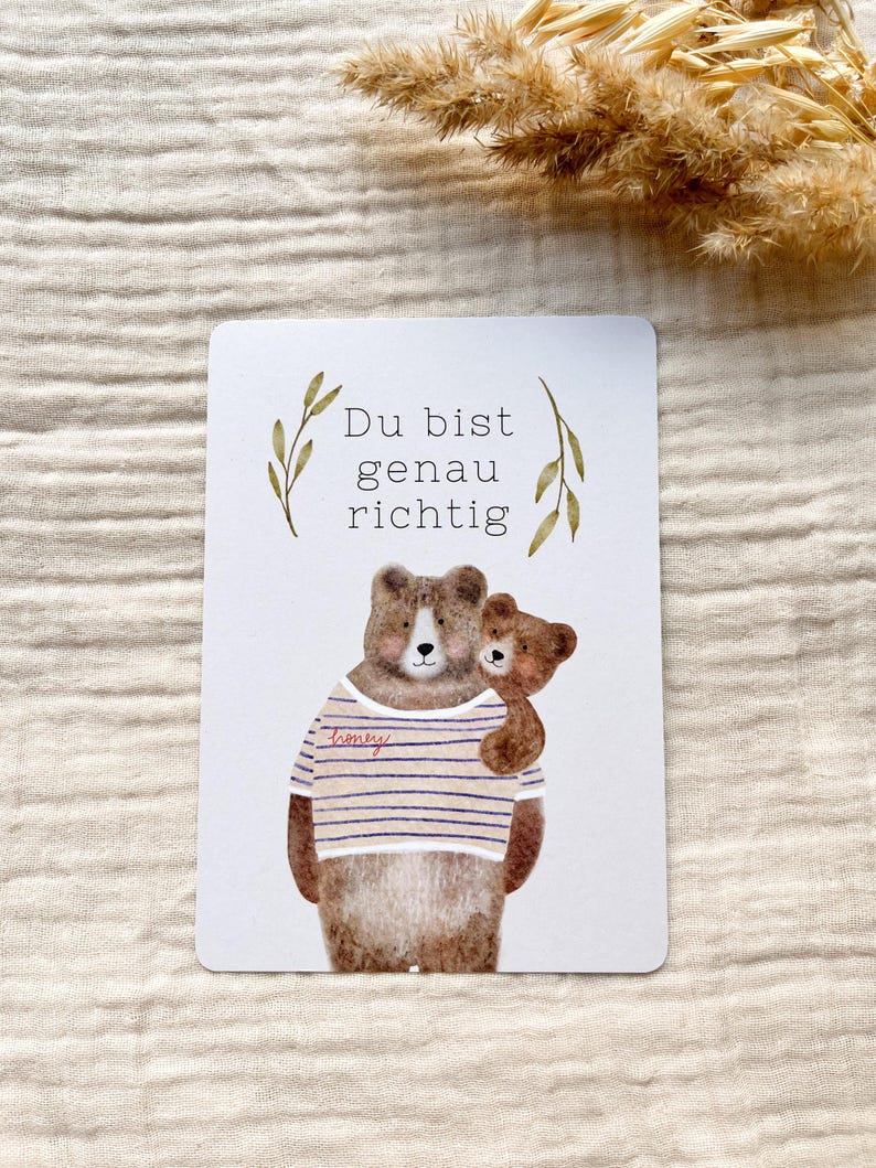 May include: A rectangular card with a watercolor illustration of two bears. The larger bear wears a striped shirt with the word "honey" on it. The smaller bear is hugging the larger bear. The text "Du bist genau richtig" is at the top.