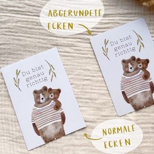 May include: Two white cards with a watercolor illustration of two bears. The larger bear wears a striped shirt and embraces a smaller bear. The text "Du bist genau richtig" is above the bears.