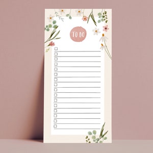 Könnte beinhalten: Ein Notizblock mit floralem Thema für eine To-Do-Liste mit hellbeigem Hintergrund. Der Notizblock hat einen rosa Kreis mit den Worten „TO DO“ und eine Reihe von Kontrollkästchen und Linien zum Schreiben. Zarte Aquarellblumen und Grün umrahmen die Ober- und Seiten.