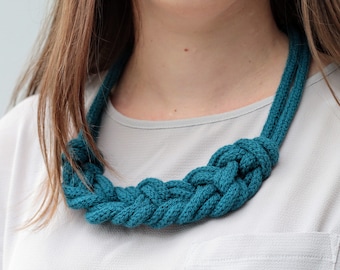 May include: A teal blue rope necklace with a knotted design. The necklace is worn by a person with long brown hair.