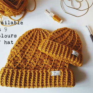 May include: Two crocheted hats in a mustard yellow color. The hats are available in nine colors. The text "Available in 9 colors of hat" is written on a white background.