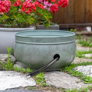 May include: A green plastic hose reel with a black hose coiled inside. The reel is sitting on a stone patio with green grass growing around it.
