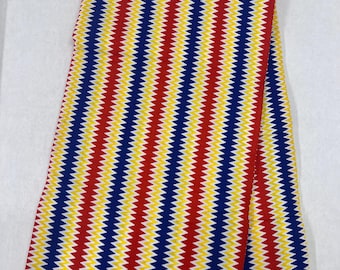 May include: Red, yellow and blue striped fabric with a zig-zag pattern. The fabric is folded and has a label that reads "Wax Block Print".
