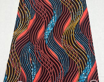 May include: A folded piece of fabric with a wavy pattern in black, blue, yellow, and orange. The fabric has the text "Guaranteed Dutch Wax" and "Veritable Wax Holland" printed on it.