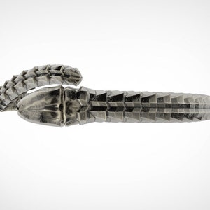 May include: A silver-colored, textured bracelet with a geometric design. The bracelet appears to be made of metal and has a detailed, scale-like pattern. The design wraps around the wrist, creating a unique accessory.