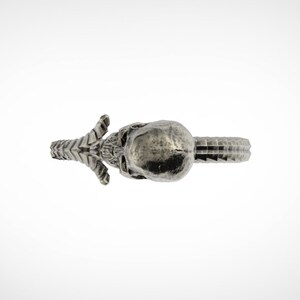 May include: A silver skull ring with a detailed design. The ring is open on one side and has a textured surface.