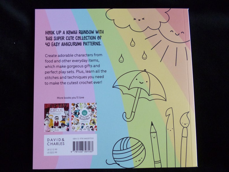 以下が含まれることがあります： 「リトルハッピーサーカス」というタイトルの書籍の後ろ表紙。虹、太陽、雲が描かれている。書籍の表紙にはバーコードと「HOOK UP A KAWAII RAINBOW WITH THIS SUPER CUTE COLLECTION OF 40 EASY AMIGURUMI PATTERNS.」というテキストが記載されている。