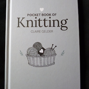 May include: A white book with the title "Pocket Book of Knitting" by Claire Gelder. The book cover features a black and white illustration of a basket of yarn with knitting needles.