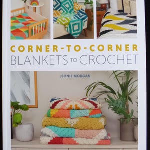 Puede incluir: Portada de libro con el título "Corner-to-Corner Blankets to Crochet" de Leonie Morgan. La portada muestra tres mantas de crochet de colores en diferentes patrones y colores, mostradas en una cama, una silla y una cuna.