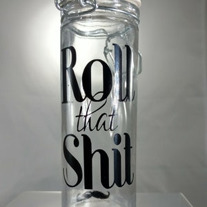 May include: Clear glass jar with a hinged lid and a black graphic that reads "Roll that Shit" with a small mustache graphic. The jar is cylindrical and appears to be empty.