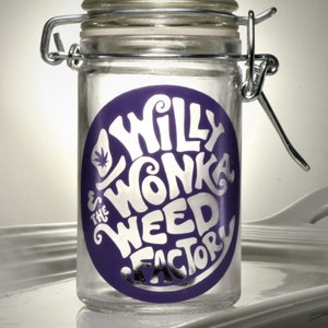 May include: A clear glass jar with a silver lid and a purple label that says "Willy Wonka The Weed Factory".