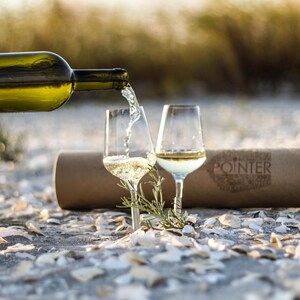 2 picnic white wine glasses pinned to the sand on the beach with white wine bottle and white wine being poured in them